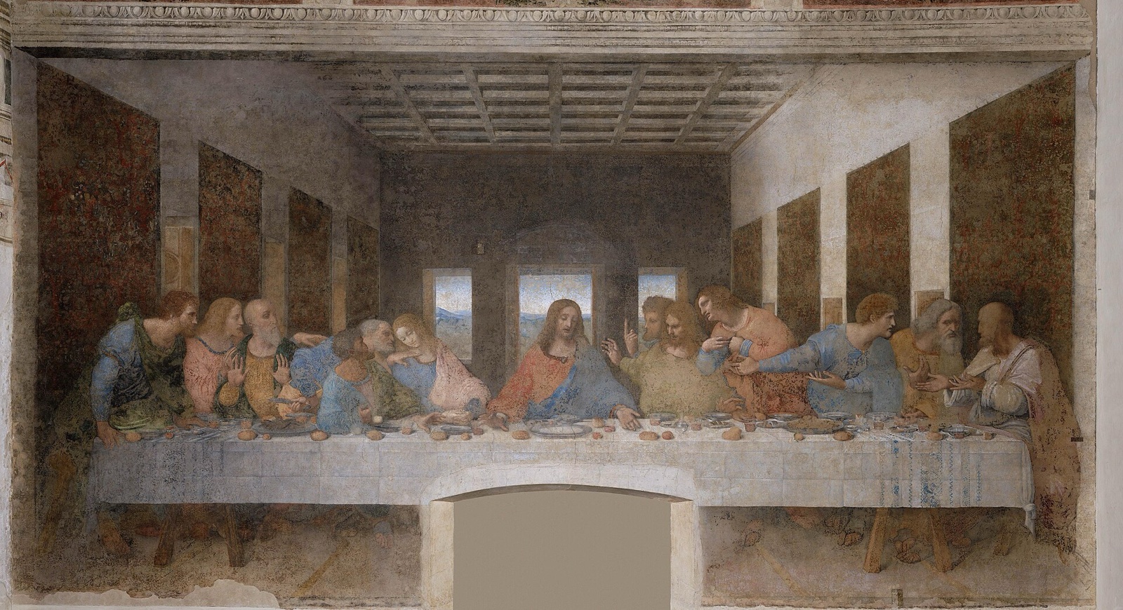 Le Christ au centre d'une longue table, entouré des douze apôtres qui réagissent par groupes de trois, dans une salle en perspective ouverte sur un paysage
