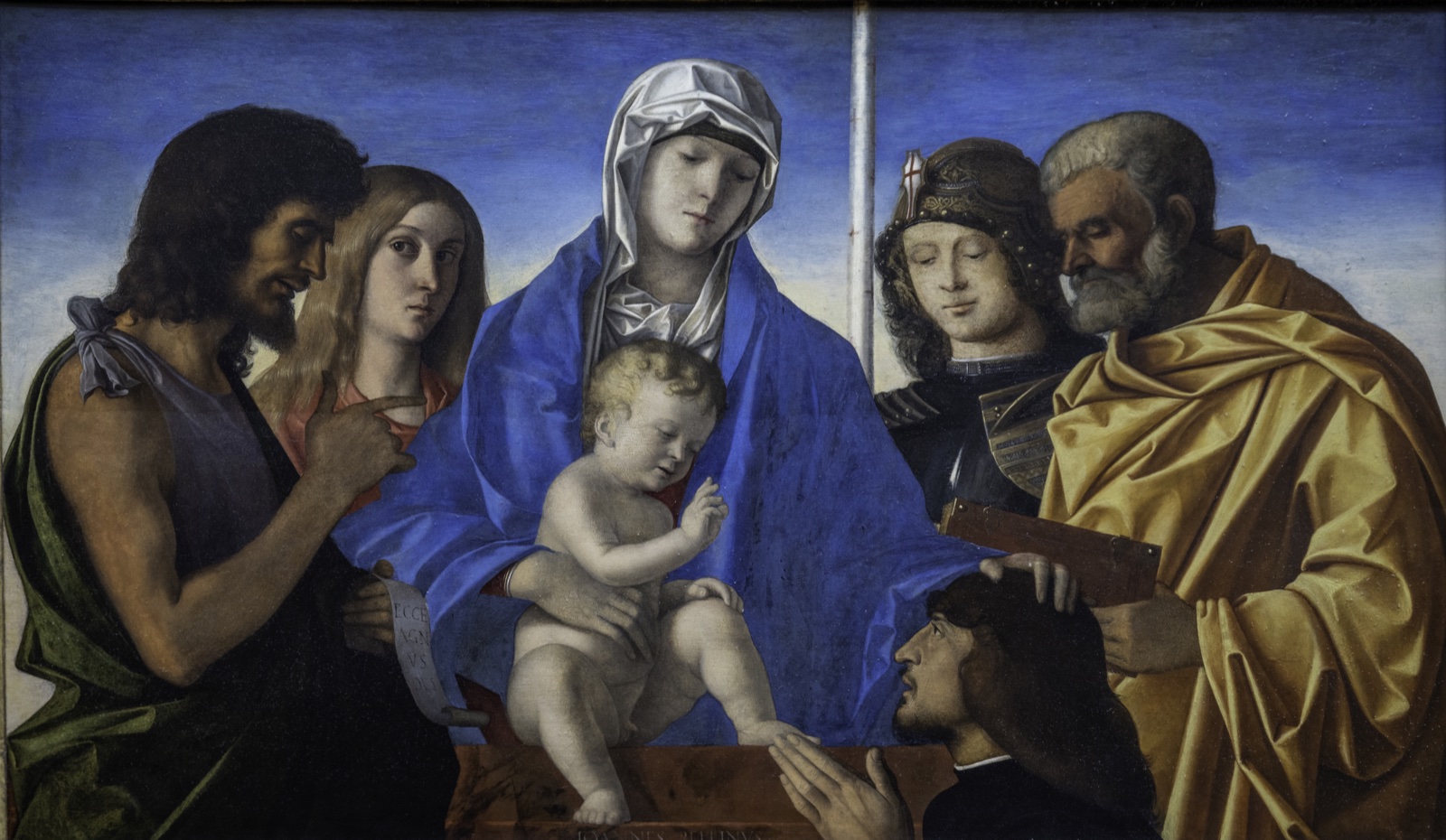 La Vierge tient l'Enfant debout sur un parapet, entourée de quatre saints ; en bas à droite, un homme en prière, la main de saint Pierre posée sur sa tête