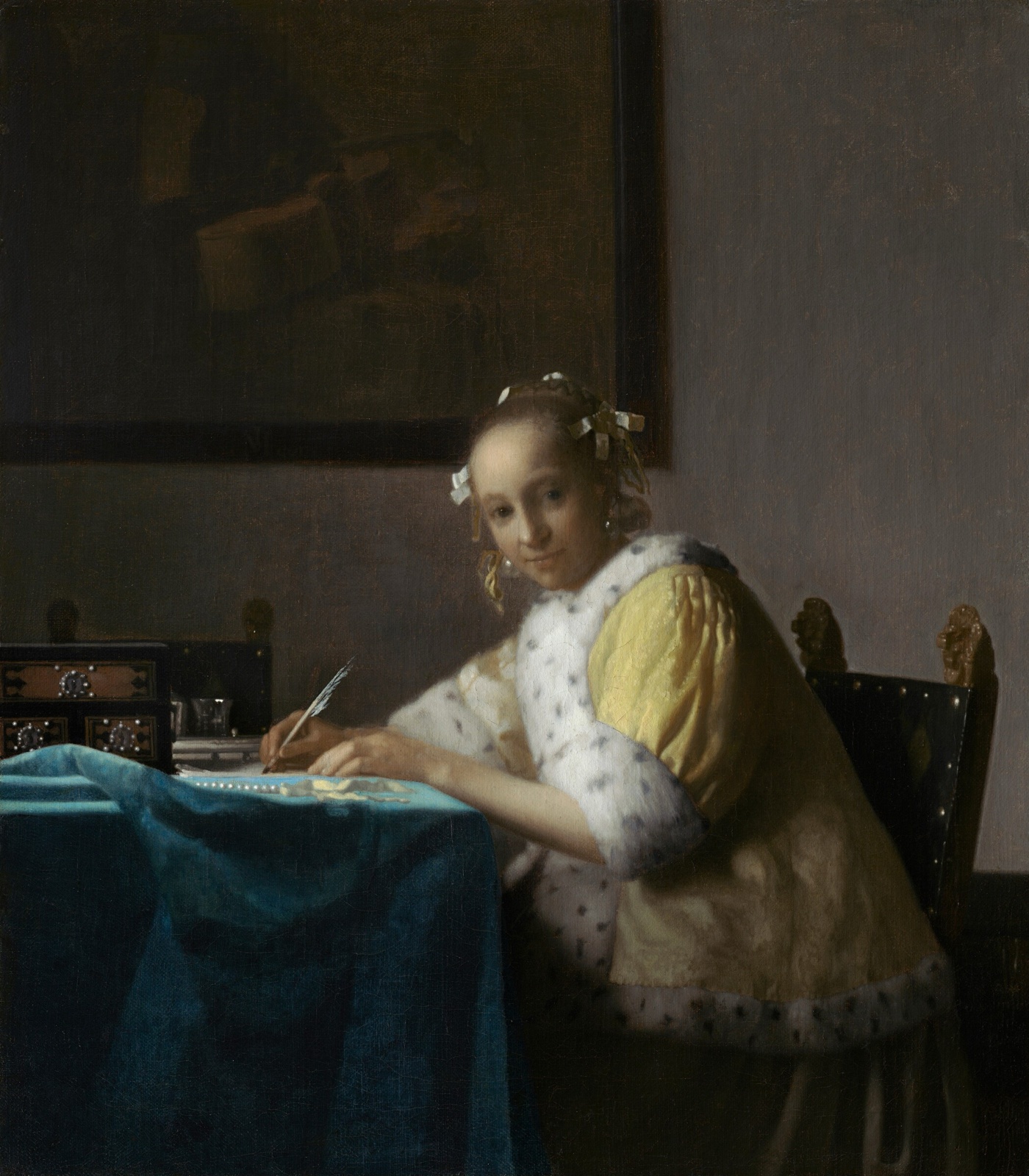 Une jeune femme en veste jaune bordée de fourrure, assise à une table couverte d'un tapis bleu, s'interrompt d'écrire et lève les yeux vers le spectateur, la plume à la main