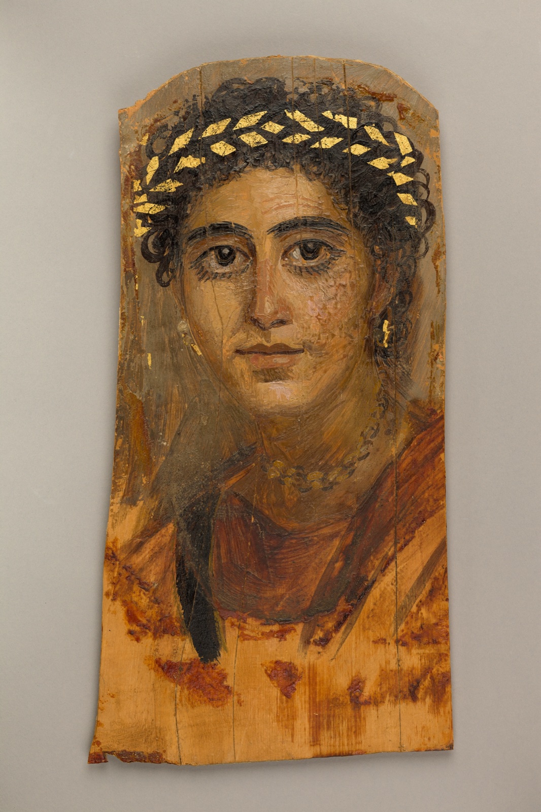 Portrait peint sur bois d'une jeune femme aux grands yeux sombres, coiffée d'une couronne de feuilles d'or, vêtue d'une tunique rouge