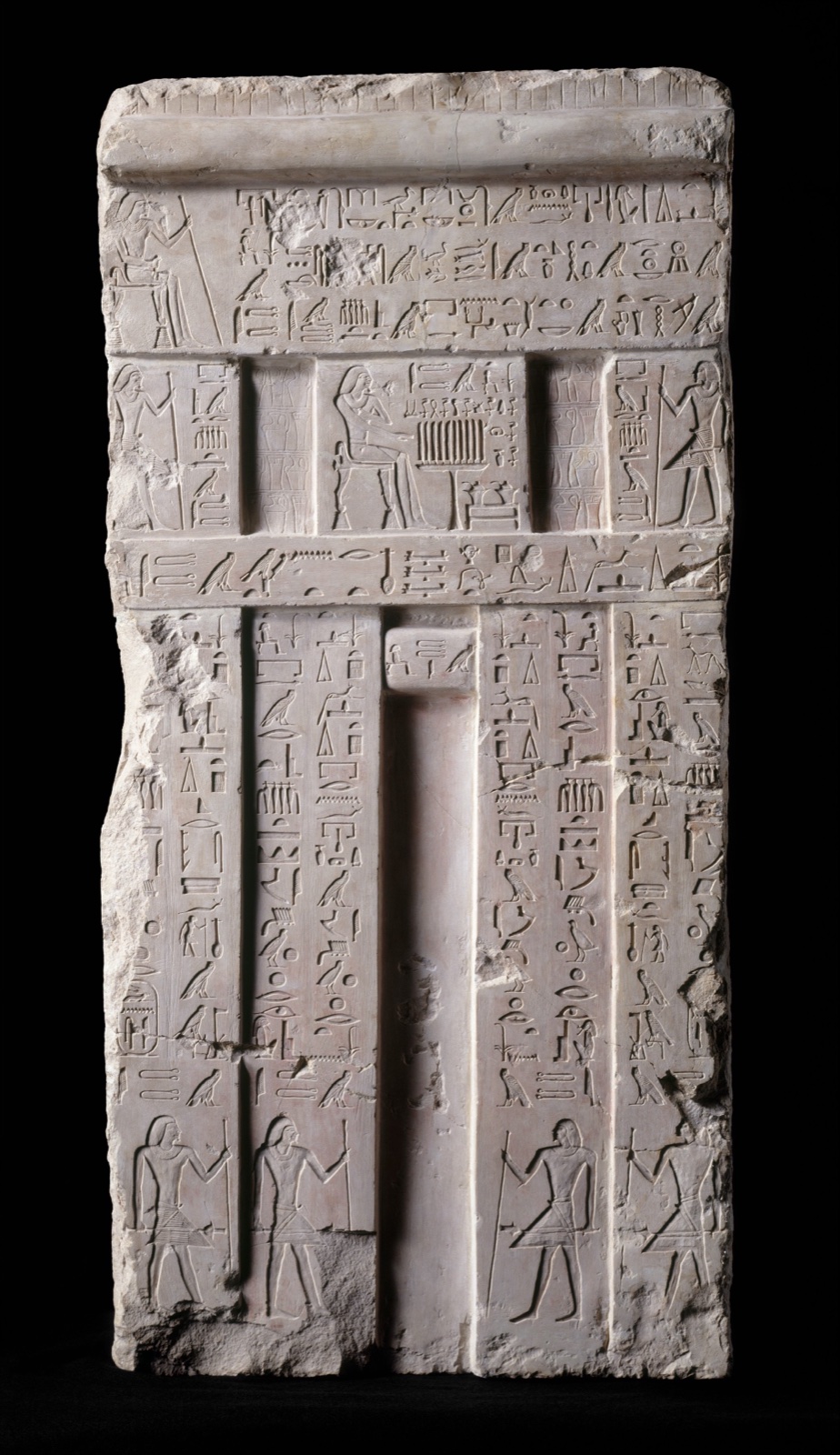 Stèle de calcaire en forme de porte, couverte de colonnes de hiéroglyphes, avec une niche étroite au centre et des personnages gravés en bas
