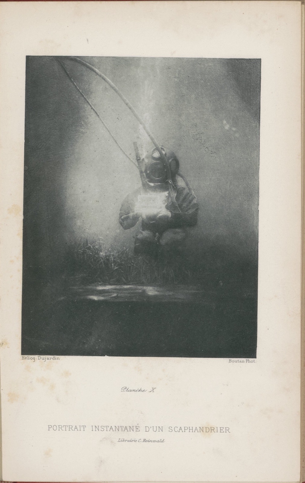 Page de livre portant une photographie sous-marine en noir et blanc : un scaphandrier casqué, relié à la surface par un tuyau, tient une plaque devant lui
