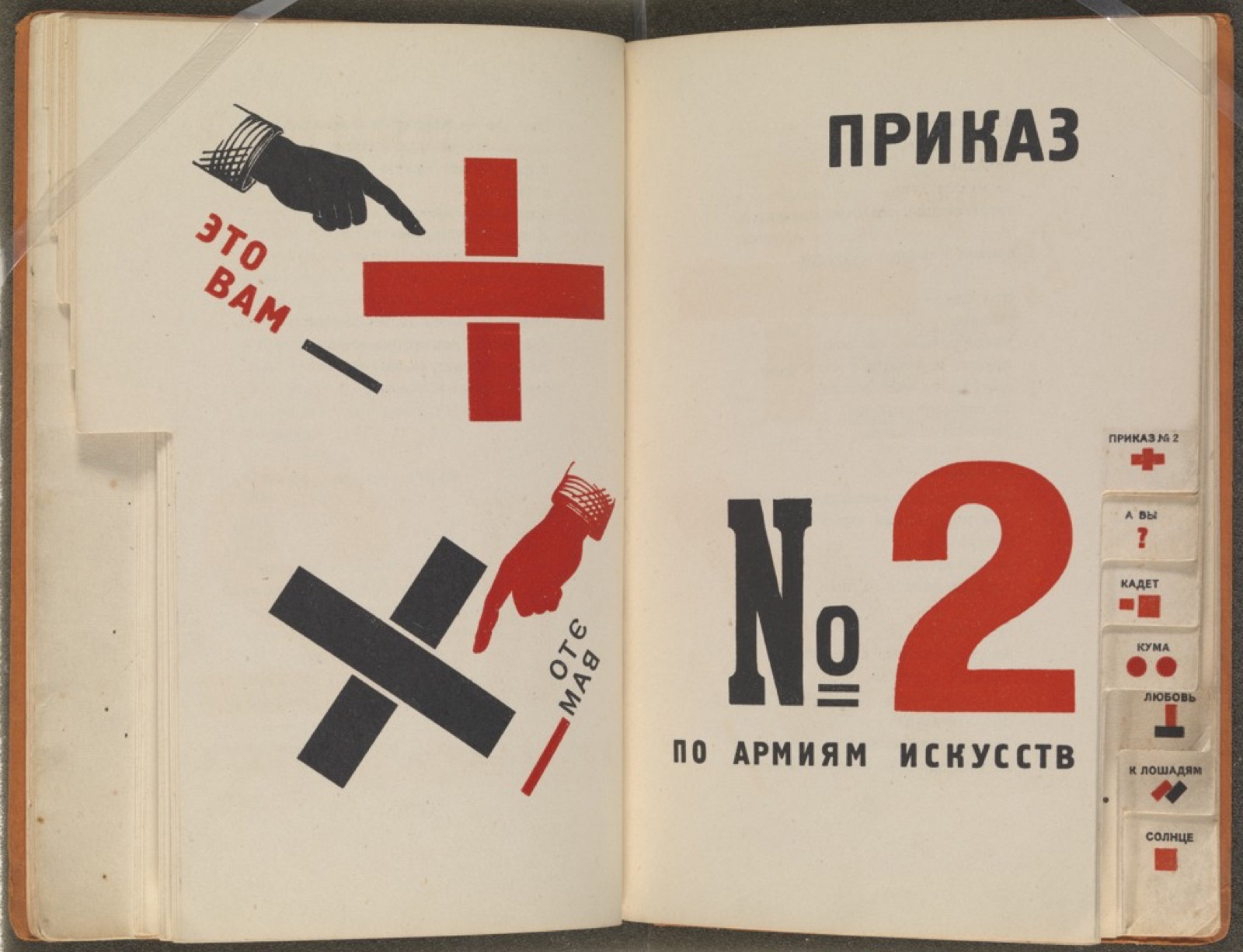 Livre ouvert : à gauche, des mains noires et rouges pointent une croix ; à droite, un grand « № 2 » rouge et noir ; sur la tranche, des onglets illustrés