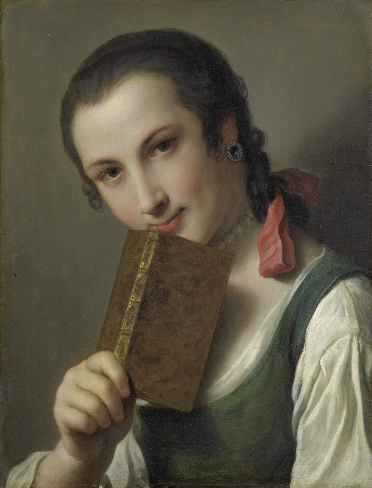 Une jeune femme aux cheveux tressés, un ruban rouge dans les cheveux, tient un petit livre relié contre son menton et regarde le spectateur