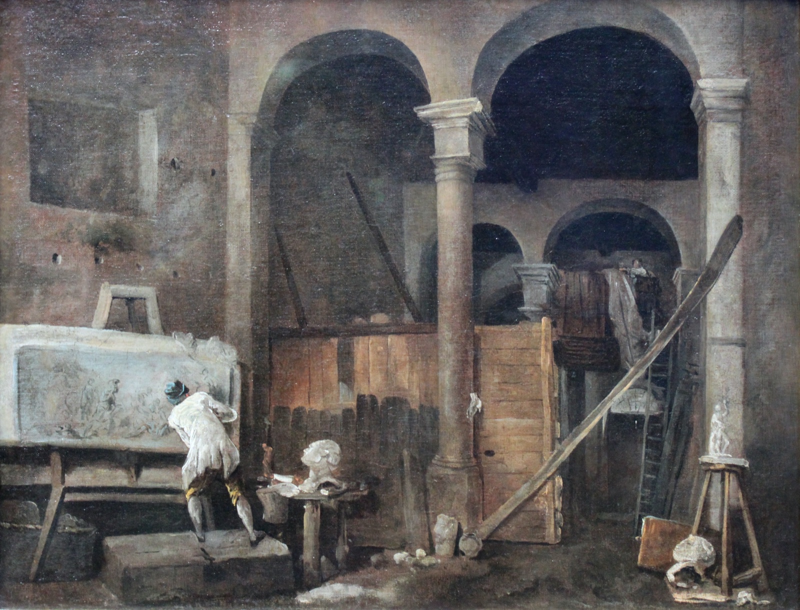 Sous des arcades, un artiste de dos travaille à un grand relief posé sur un chevalet, au milieu de bustes, d'échelles et de planches