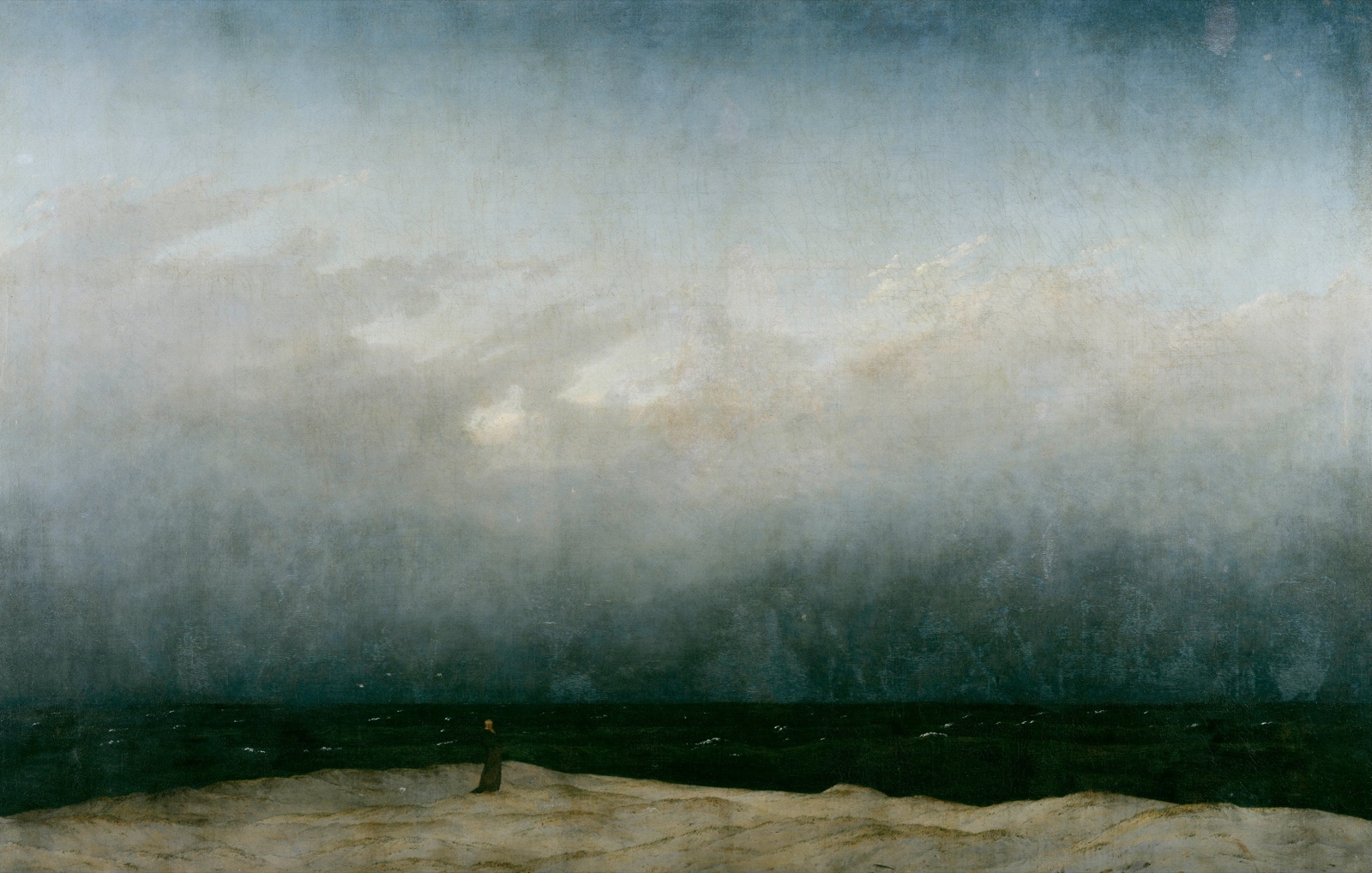 Une minuscule silhouette de moine debout sur une dune claire, face à une mer sombre et à un immense ciel brumeux