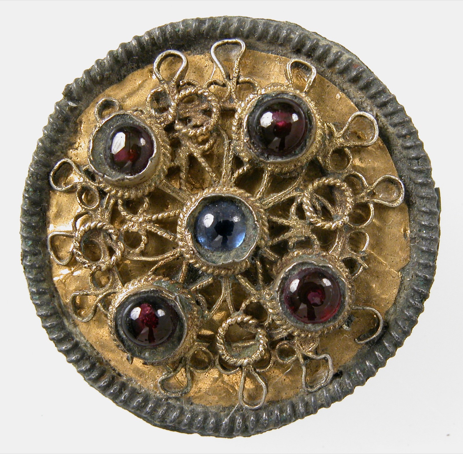 Petite broche ronde dorée, couverte de fils d'or en volutes, sertie de quatre grenats rouges autour d'un saphir bleu